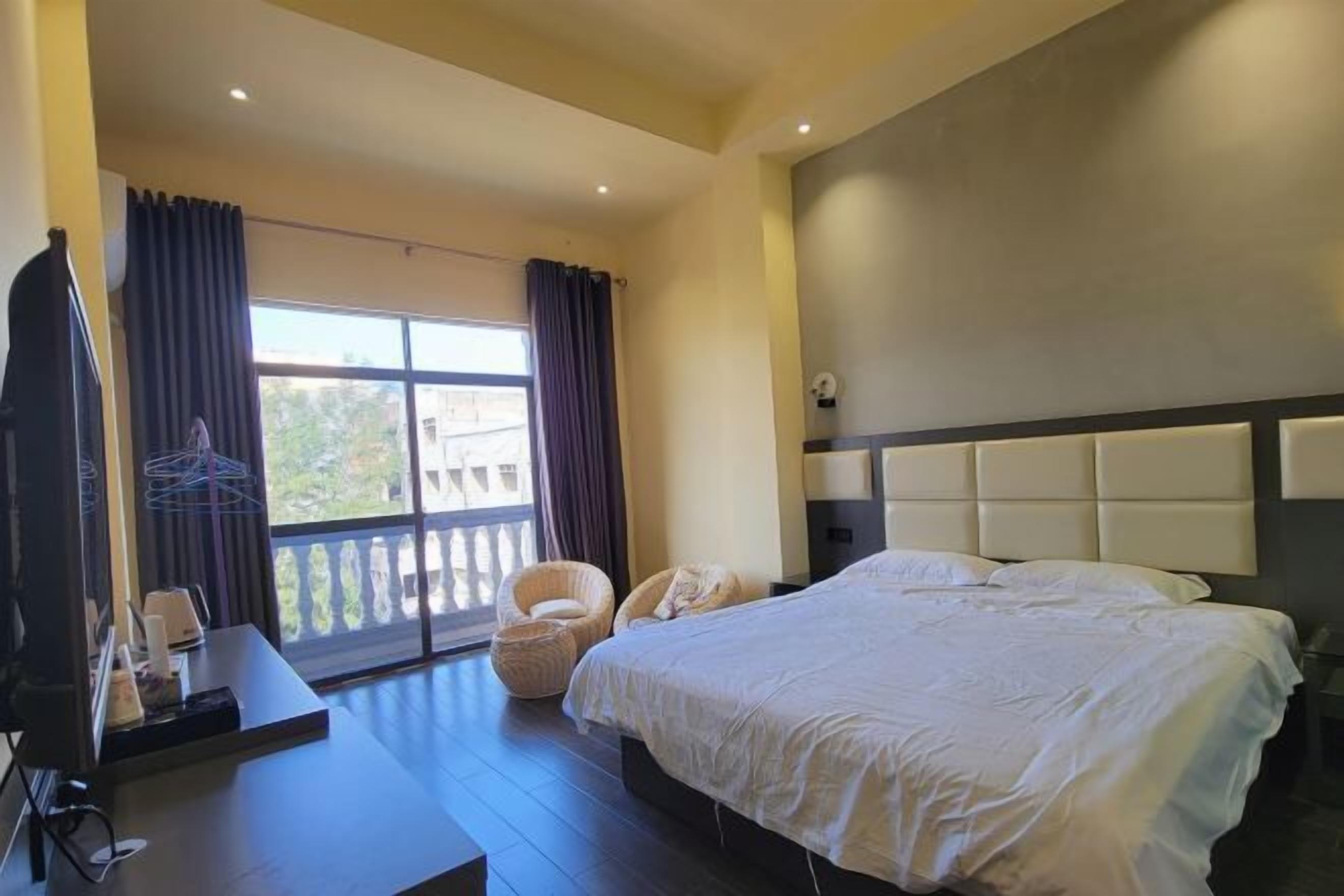 Een hotelkamer met een groot bed, een bureau en een stoel. Er is een balkon met gordijnen en uitzicht op buiten.