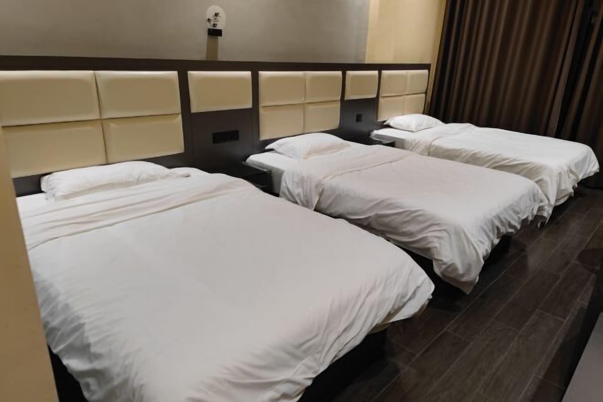 Een hotelkamer met drie eenpersoonsbedden, een hoofdbord met een lichtgekleurd paneel en een donkere houten vloer.