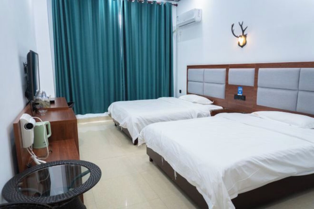 A hotel room with two beds, a desk with a chair, a TV, and a wall-mounted deer head light.