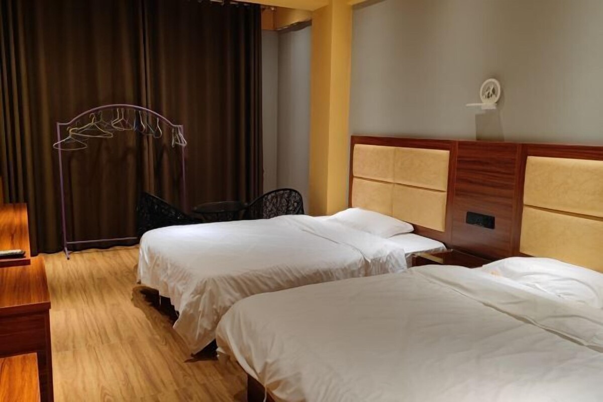 Een hotelkamer met twee bedden, een houten vloer, een hoofdeinde met opbergruimte en een gordijn.