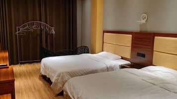 Een hotelkamer met twee bedden, een houten vloer, een hoofdeinde met opbergruimte en een gordijn.