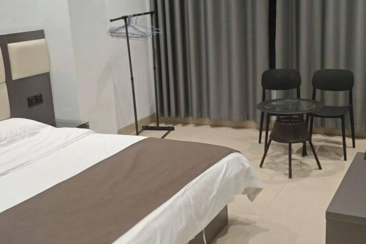 Ein Hotelzimmer mit Bett, Nachttisch, Sessel, rundem Tisch und Vorhang.