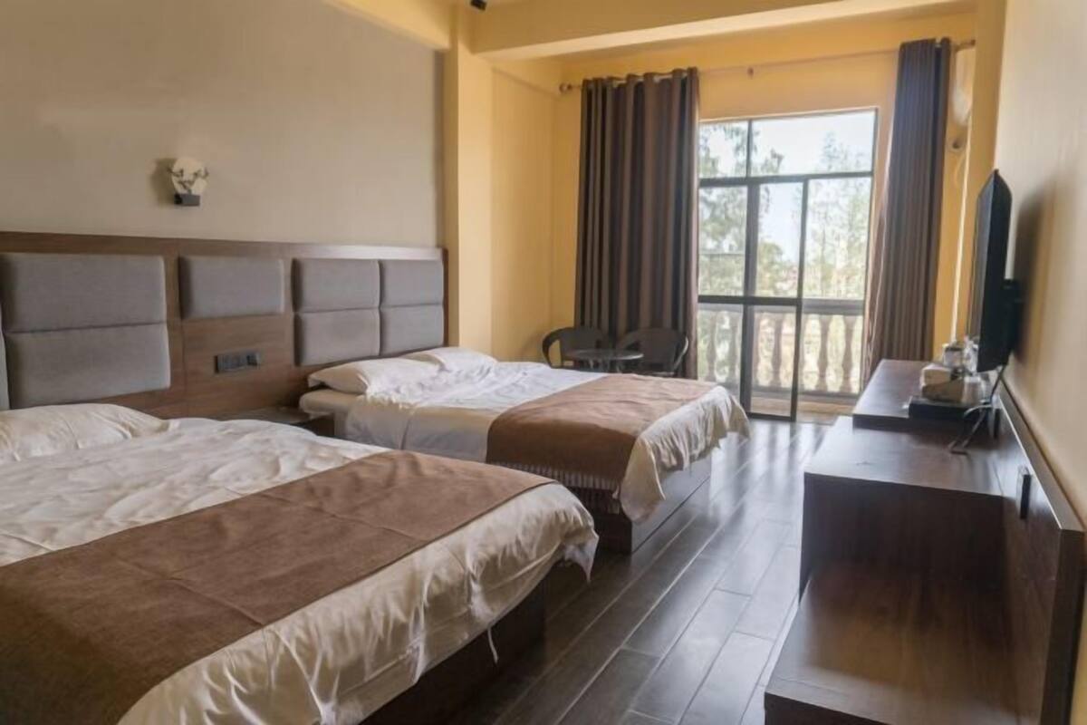 Ein Hotelzimmer mit zwei Betten, einem Schreibtisch, einem Stuhl, einem Fernseher und einem Fenster mit Vorhängen.