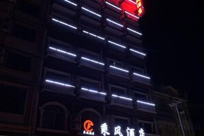 Een meerhoog gebouw met verlichte balkons en een opvallend bord bovenop.