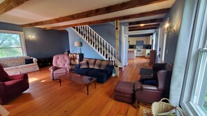 Un salon spacieux avec un escalier en bois, un canapé bleu, un fauteuil rouge et une bibliothèque.