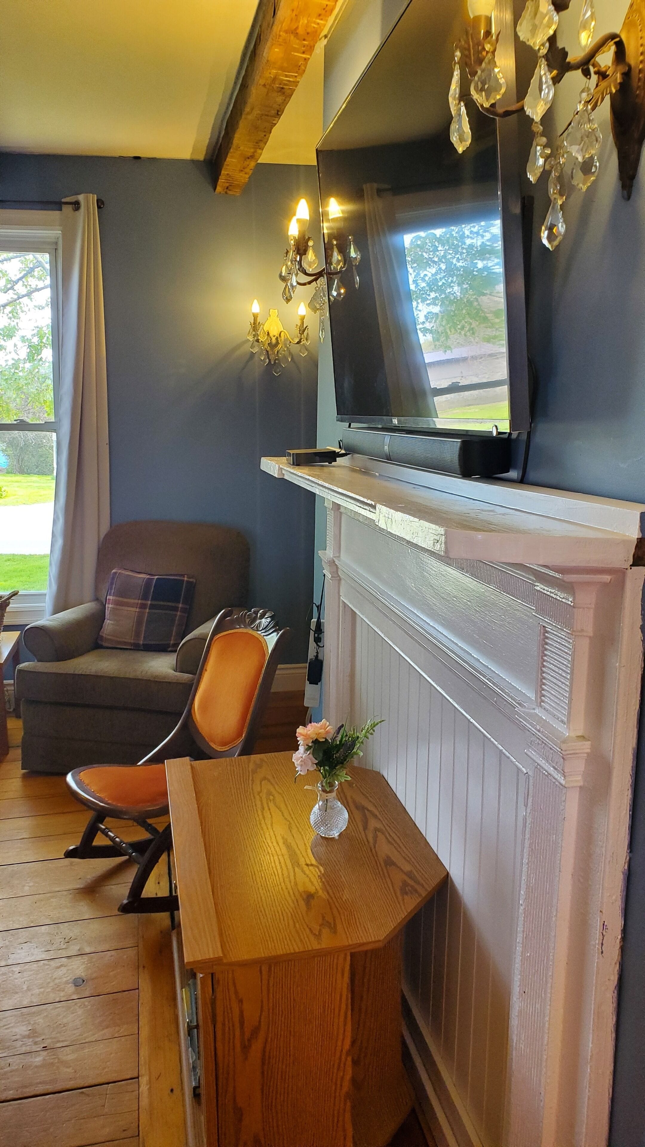 A cozy room with a fireplace, a television mounted above it, and a comfortable seating area with a chair and a table.