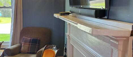 A cozy room with a fireplace, a television mounted above it, and a comfortable seating area with a chair and a table.
