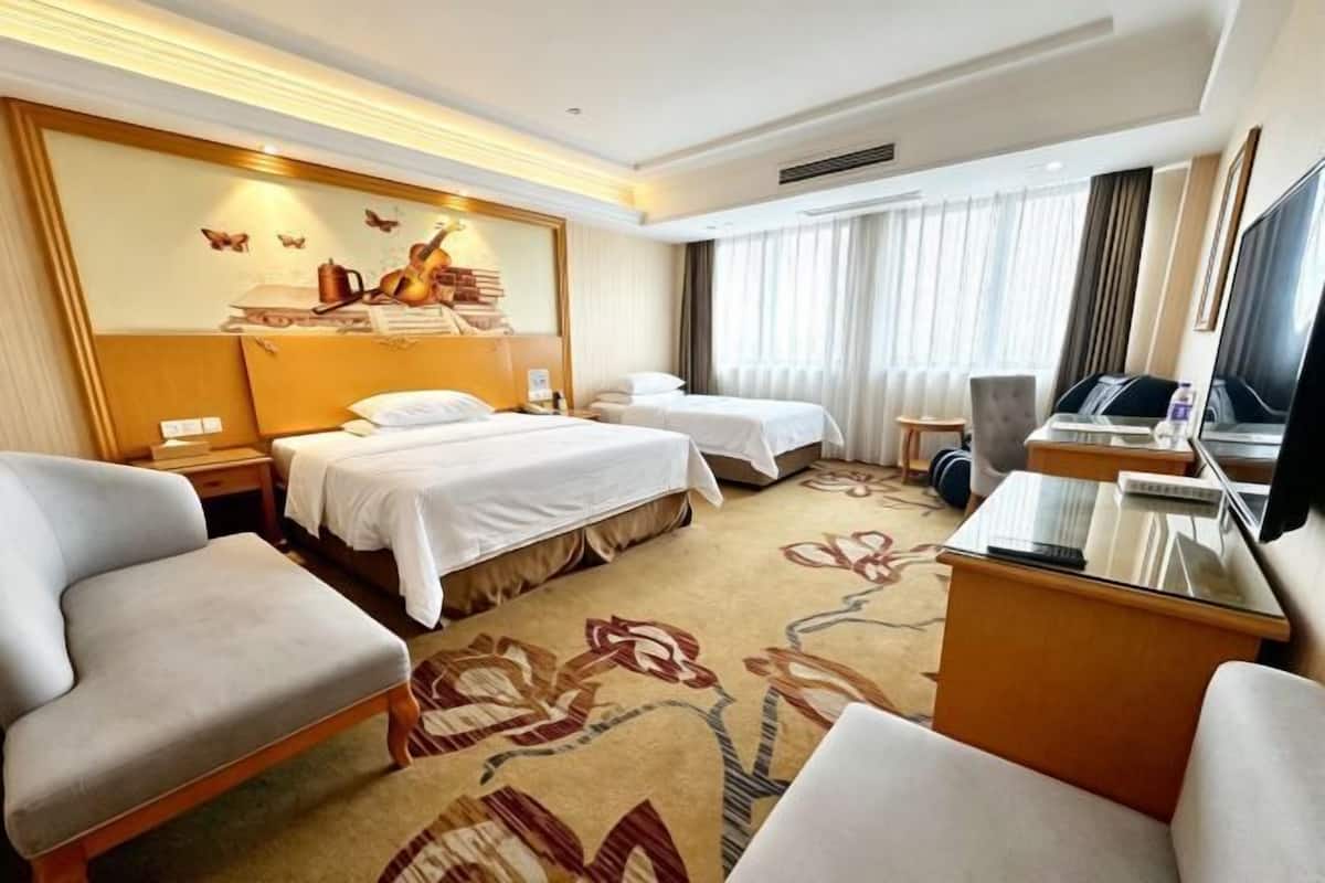A hotel room with two beds, a desk, a TV, and a seating area.