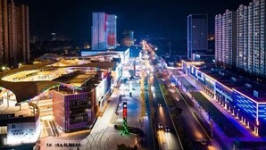 Un paisaje urbano nocturno con edificios modernos, una estructura curva con techo y una calle concurrida con vehículos.