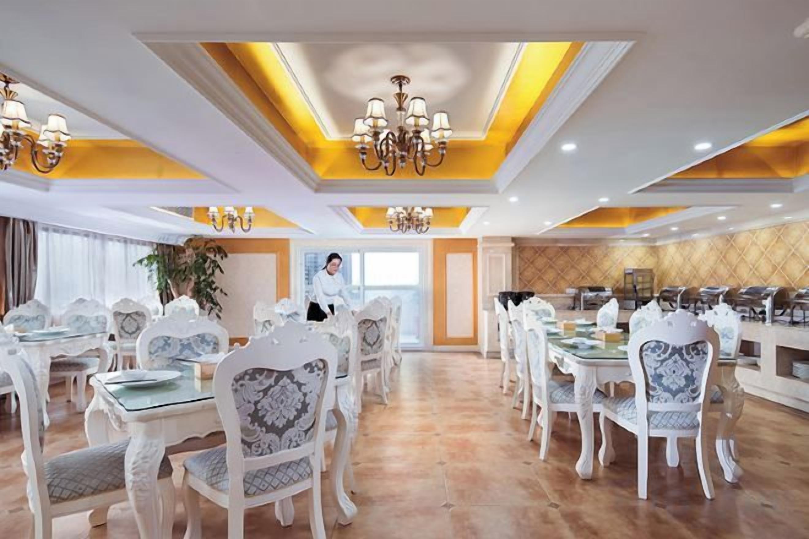 Un comedor espacioso con varias mesas y sillas, un candelabro y una persona al fondo.