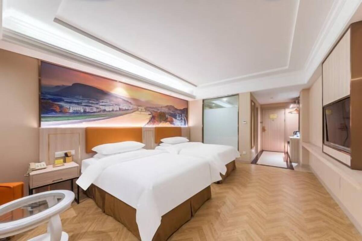Quarto de hotel com uma cama grande, uma escrivaninha, uma cadeira, uma televisão e um quadro na parede.