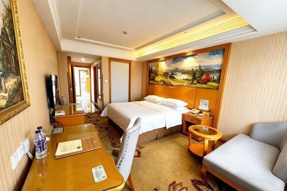 A hotel room with a bed, a desk, a chair, a TV, a painting, and a window.