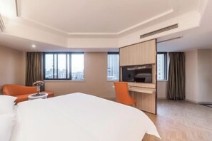 A hotel room with a bed, a desk with a TV, a chair, and a view of the city through large windows. - Vienna Hotel (Taixing Gulou Xintiandi Sports Center) (Taixing)
