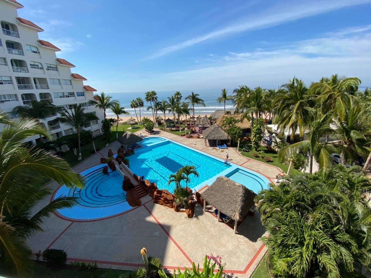 A resort with a large swimming pool, palm trees, and a view of the ocean.