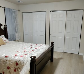 Une chambre à coucher avec un lit, une tête de lit en bois, une fenêtre avec des rideaux et deux portes blanches.