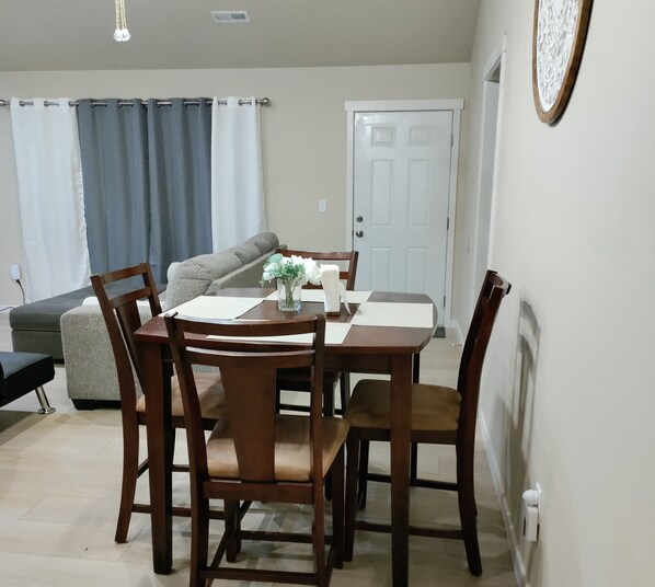 Un coin repas avec une table et des chaises en bois, un vase rempli de fleurs et un canapé en arrière-plan.