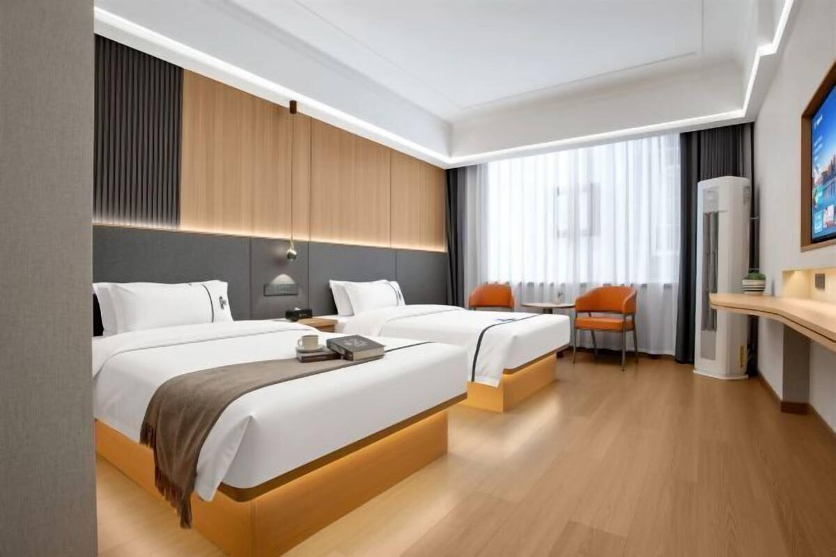 Una habitación de hotel moderna con dos camas, una zona de estar y un ventanal grande.