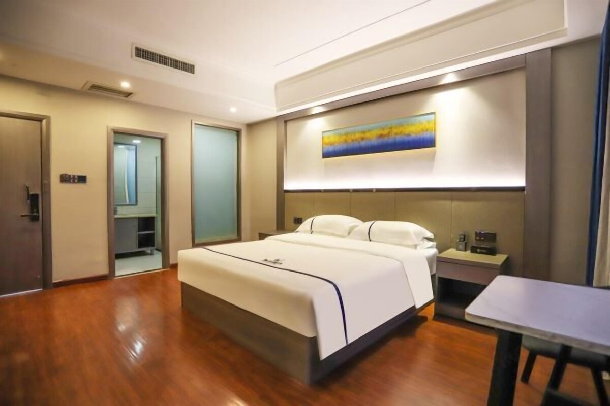 A modern hotel room with a large bed, bedside table, and a painting on the wall.