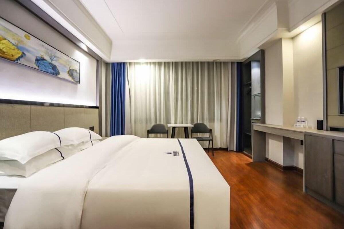 A hotel room with a large bed, a desk, a chair, a small table, and a painting on the wall.