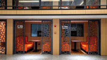 A hotel lobby with a modern design, featuring a glass partition with a geometric pattern, a reception desk, and seating areas with orange chairs.