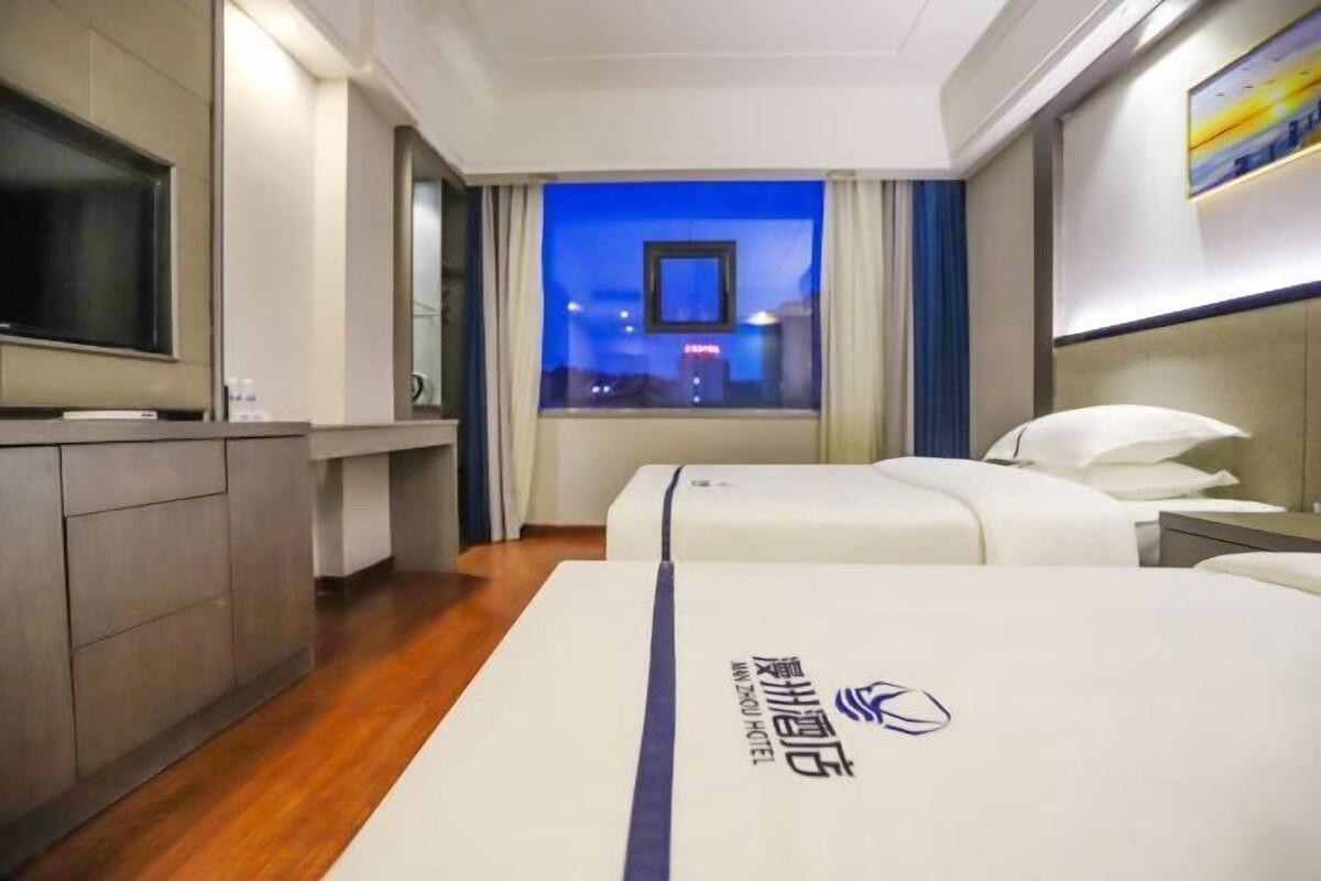 A hotel room with a bed, a TV, a window with curtains, and a night view outside.