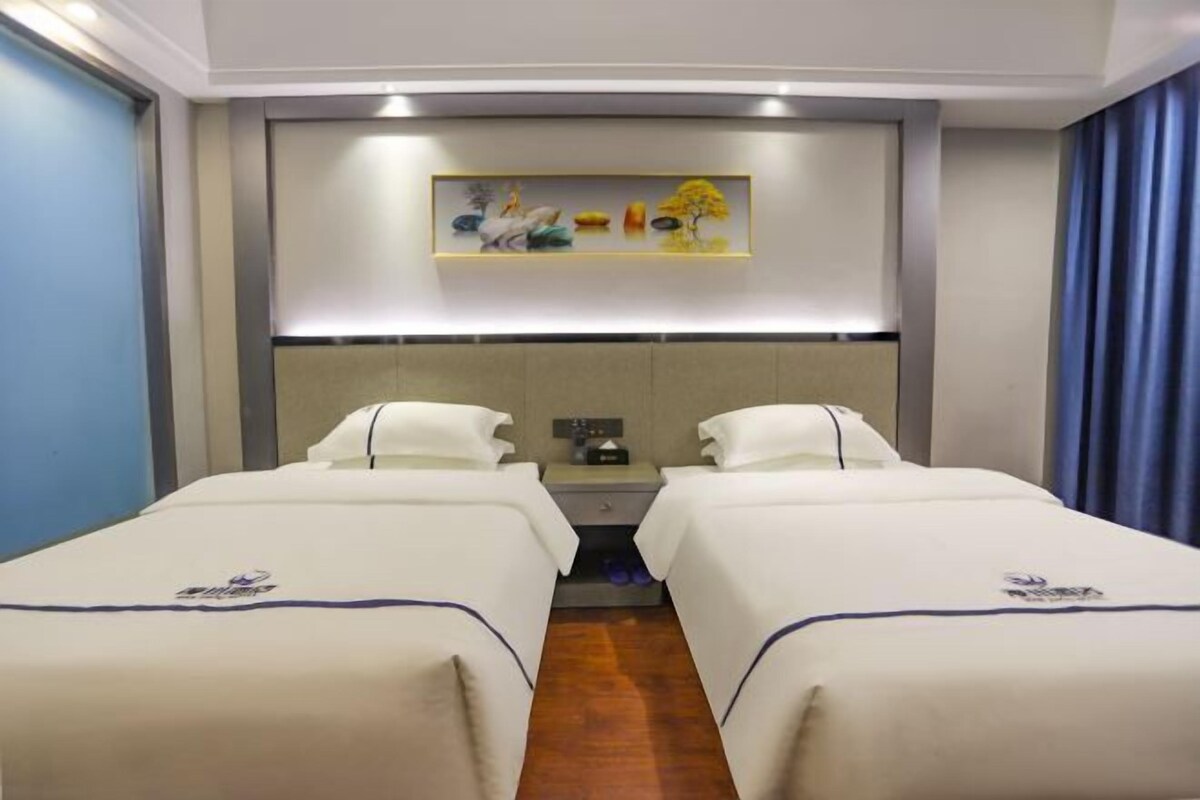 A hotel room with two beds, a nightstand, a painting on the wall, and a blue curtain.