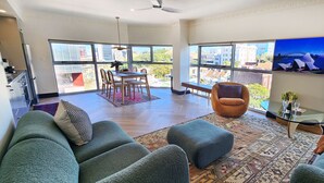 A spacious living room with a large sofa, a dining area with a table and chairs, and a view of the city through large windows. - Chic penthouse apartment in heart of Darlinghurst (Darlinghurst)
