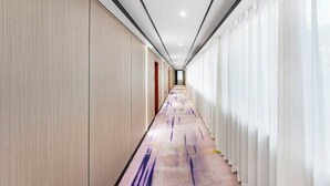A modern hotel corridor with a long, narrow layout, featuring a light-colored wooden wall on one side and a white curtain-covered wall on the other. - Junxing hotel (Yingde)