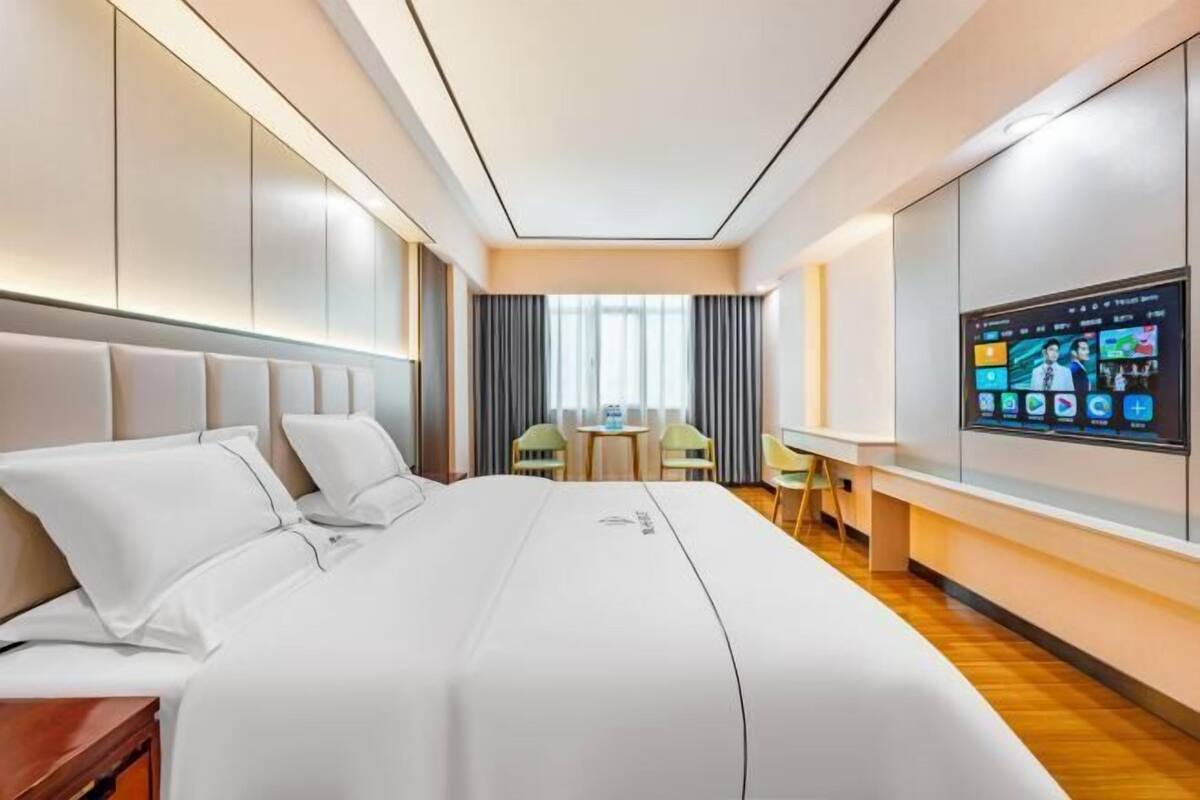 Una habitación de hotel moderna con una cama grande, un escritorio y un televisor mostrando varios canales.