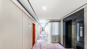 A hotel corridor with a patterned carpet, doors, and an elevator. - Junxing hotel (Yingde)
