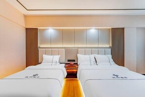 A hotel room with two beds, a wooden floor, a modern headboard, and a bedside table with a lamp. - Junxing hotel (Yingde)