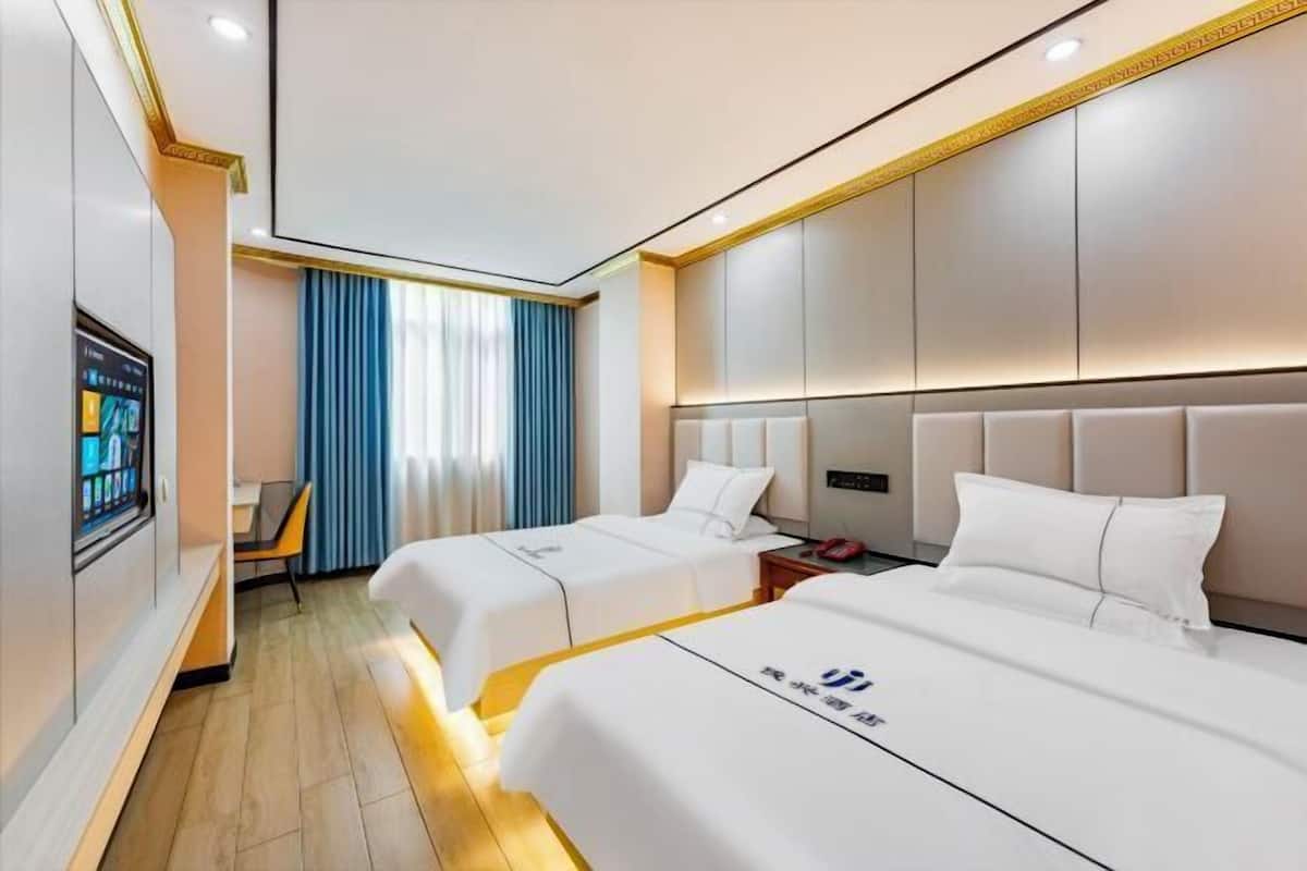 Habitación de hotel con dos camas, televisión, escritorio y ventana con cortinas.