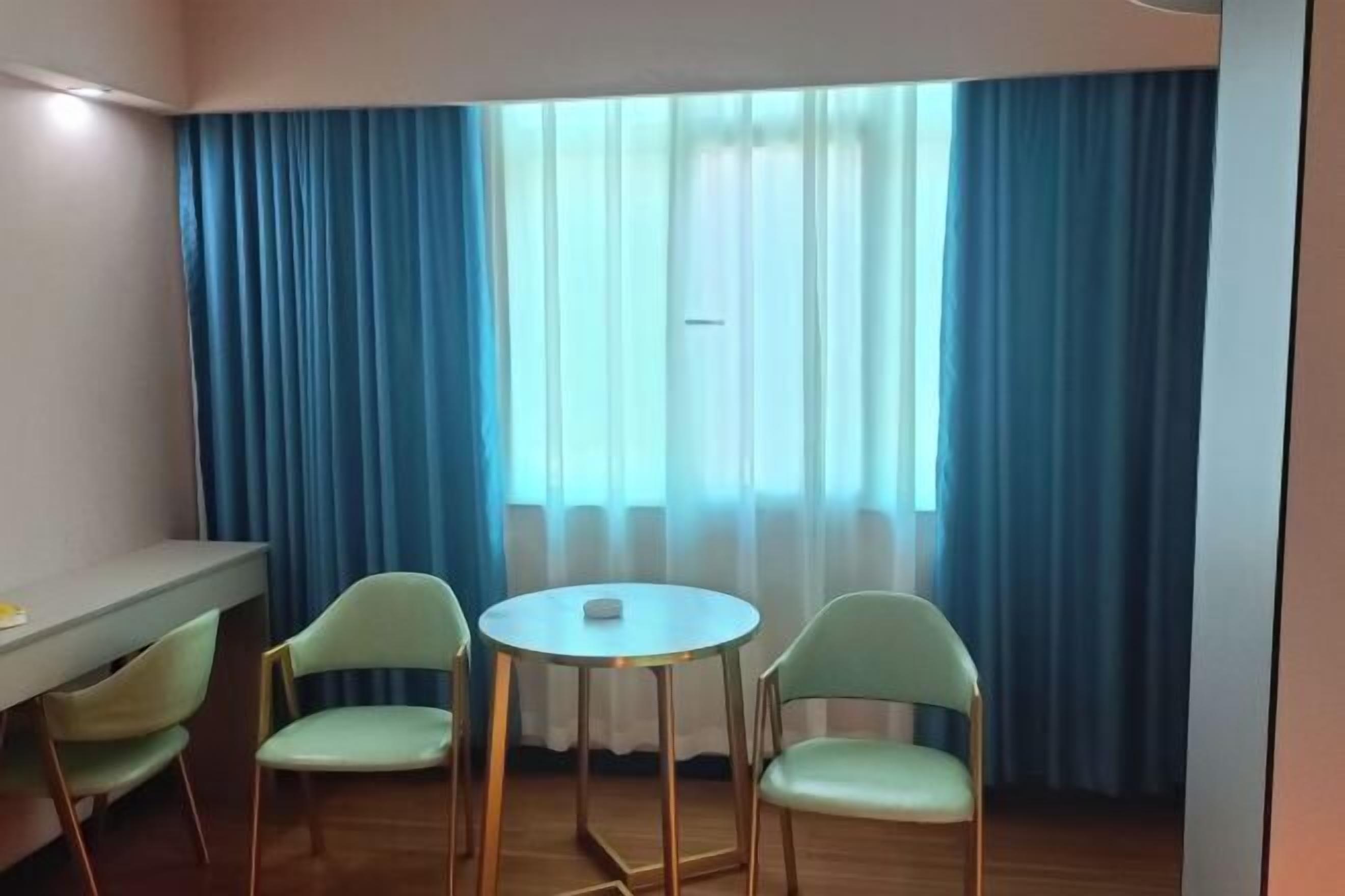 A room with a small round table and two chairs, a desk with a chair, and a window with blue curtains.