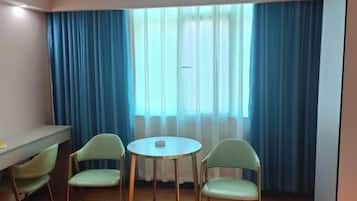A room with a small round table and two chairs, a desk with a chair, and a window with blue curtains.