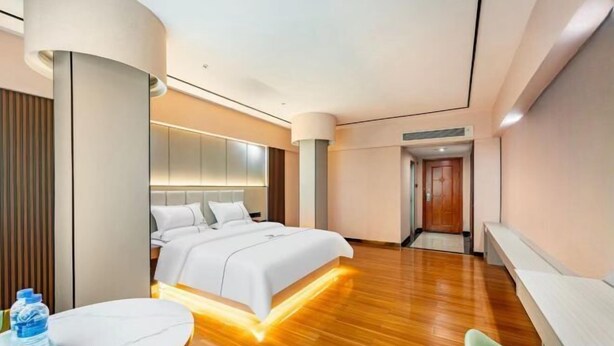 A modern hotel room with a bed, a table, a chair, and a water bottle. - Junxing hotel (Yingde)