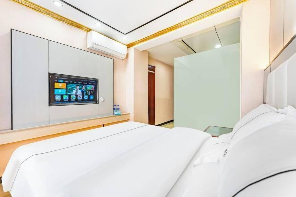 Una habitación de hotel moderna con una cama grande, un televisor integrado mostrando la pantalla de inicio y un armario con puertas correderas.