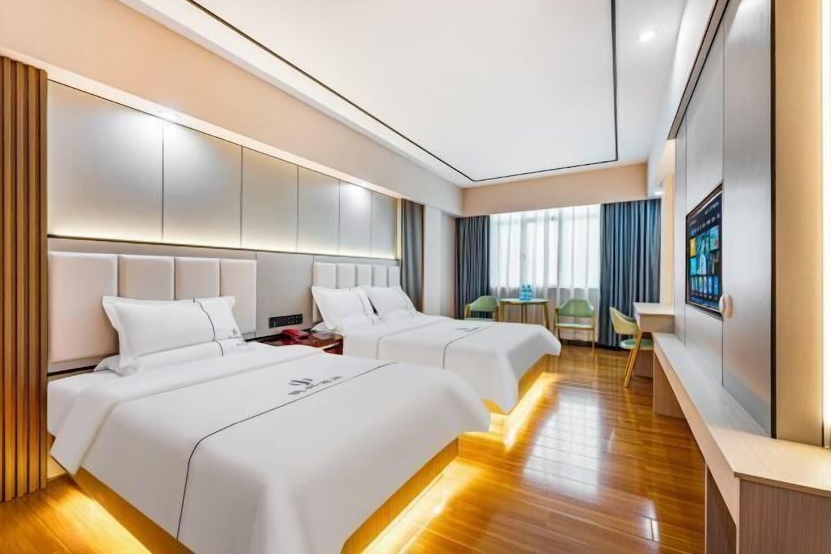 A hotel room with two beds, a desk, a chair, and a TV.
