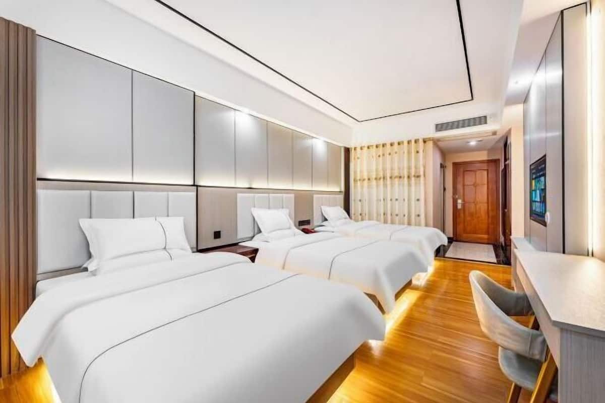 Habitación de hotel con tres camas, piso de madera y diseño moderno.