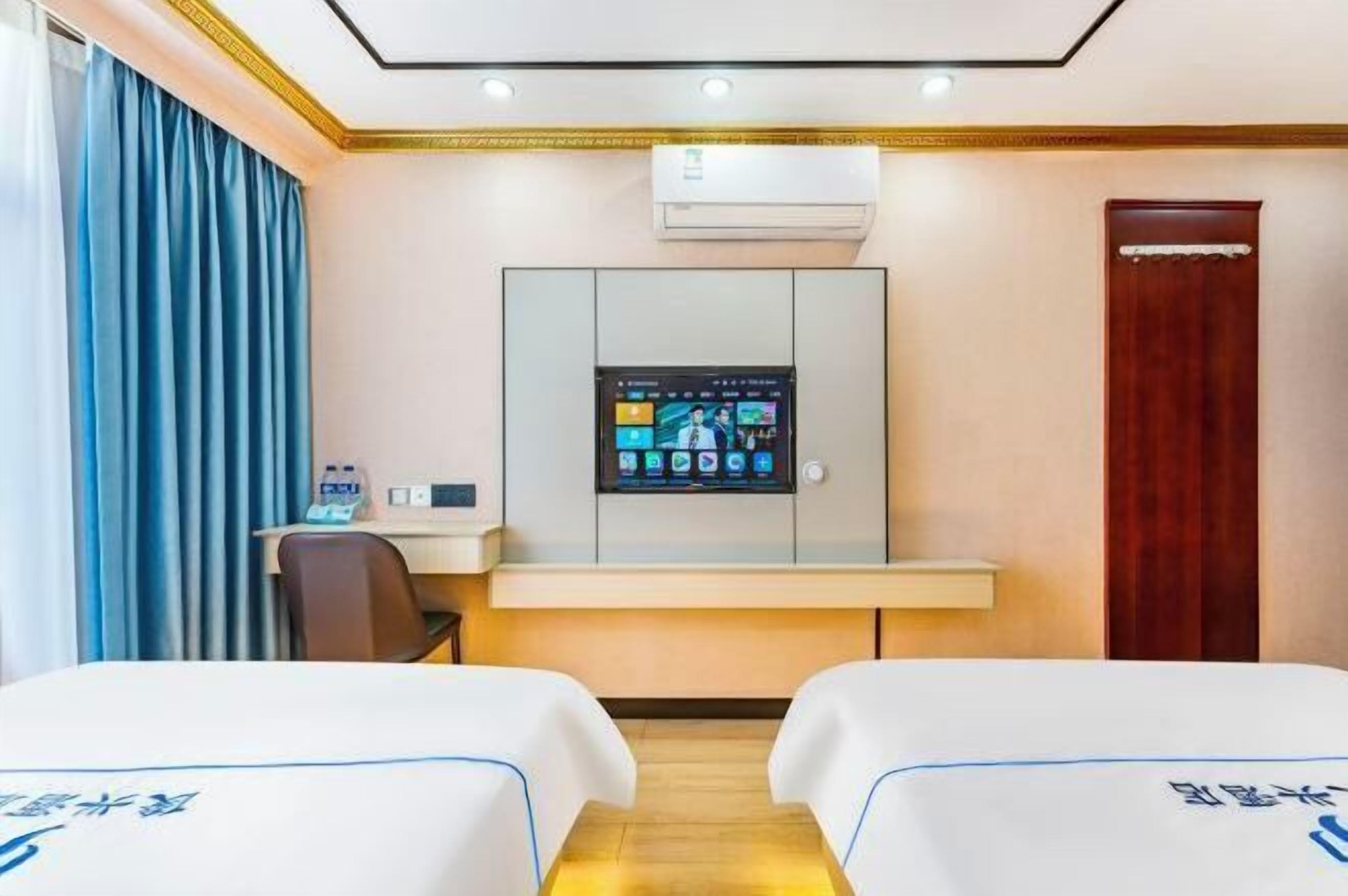 Habitación de hotel con dos camas, un escritorio con ordenador, aire acondicionado y una puerta de madera.