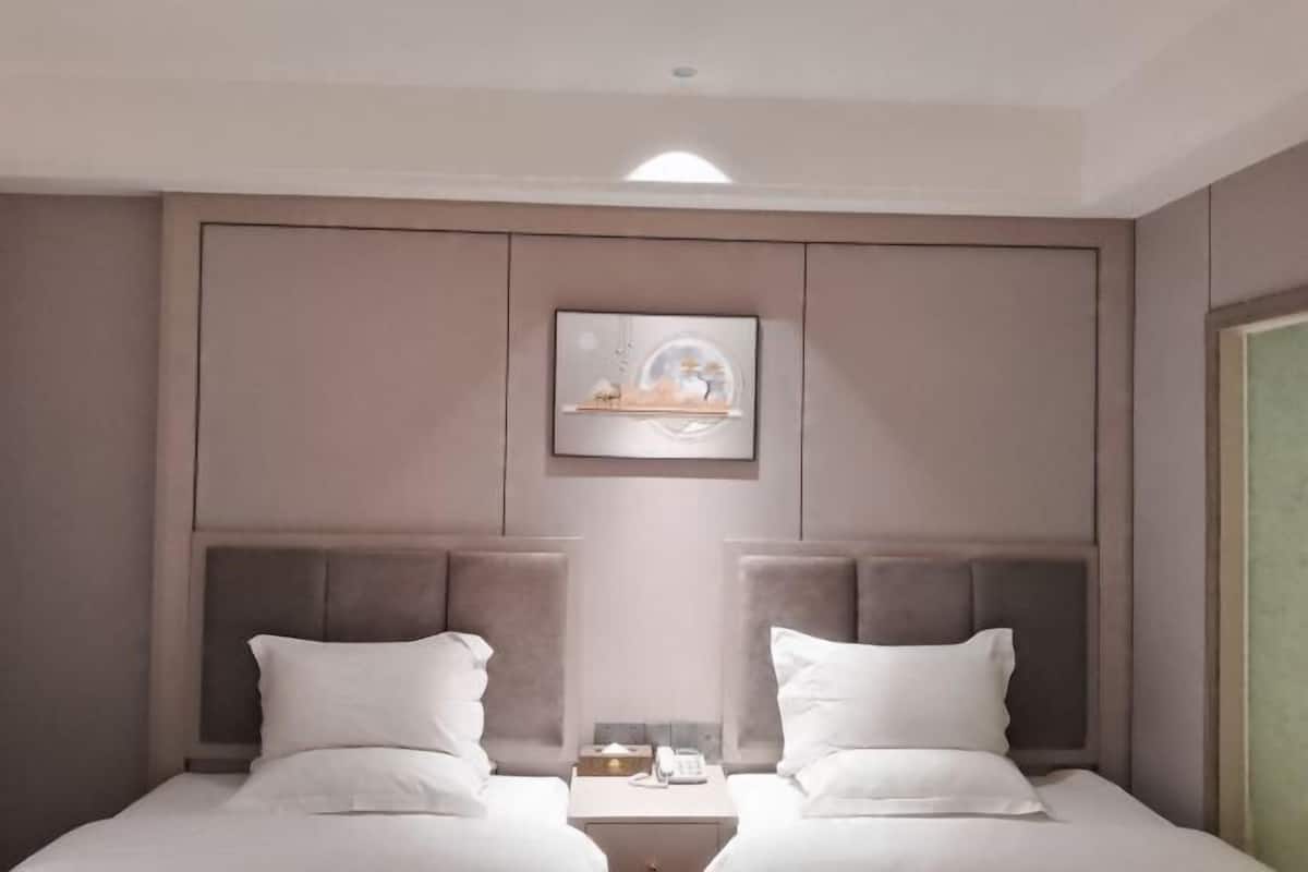 A hotel room with two beds, a nightstand between them, a framed picture on the wall, and a ceiling light.
