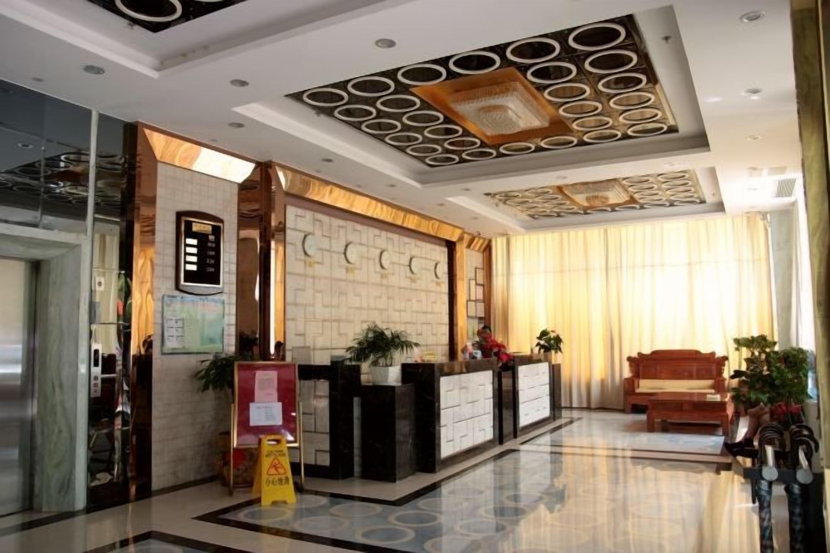 A hotel lobby with a reception desk, a wooden bench, and a large window with curtains.