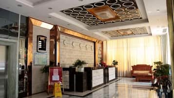 A hotel lobby with a reception desk, a wooden bench, and a large window with curtains.