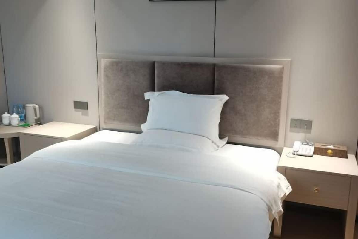 A hotel room with a bed, a nightstand, a telephone, and a small table with a water bottle and a cup.