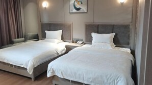 Quarto de hotel com duas camas, uma mesa de cabeceira com telefone, uma luminária na parede e um quadro.