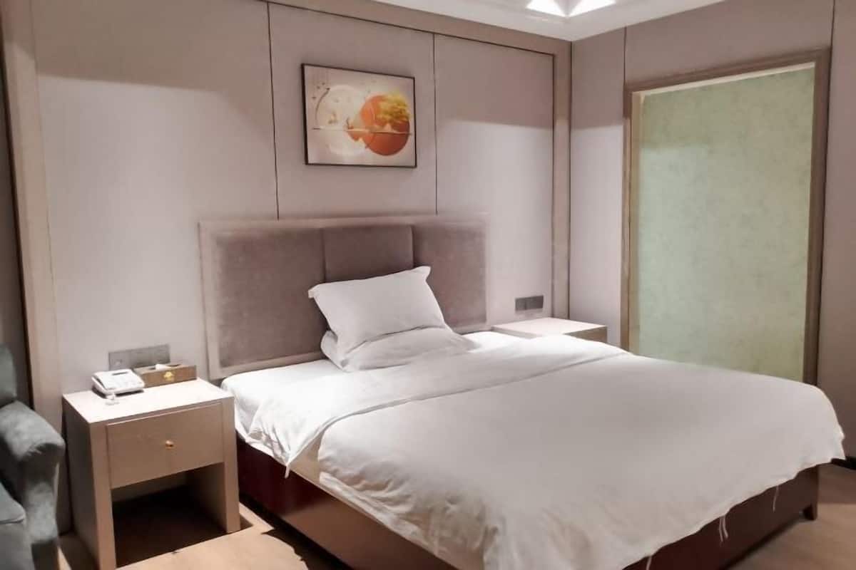 A modern hotel room with a bed, a nightstand, a chair, and a wall-mounted artwork.