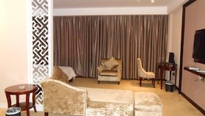 Quarto de hotel com sofá, duas poltronas, uma mesinha, televisão e cortina.