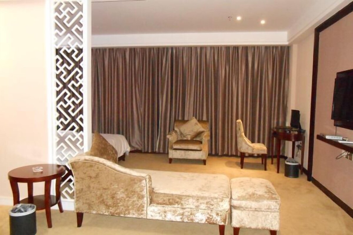 A hotel room with a sofa, two armchairs, a small table, a TV, and a curtain.