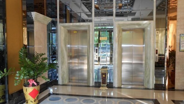 Um hall de entrada com piso de mármore, uma planta em vaso e uma porta de vidro que dá acesso aos elevadores.