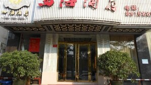 Entrada de hotel com uma placa em caracteres chineses, um número de telefone e duas plantas em vasos.