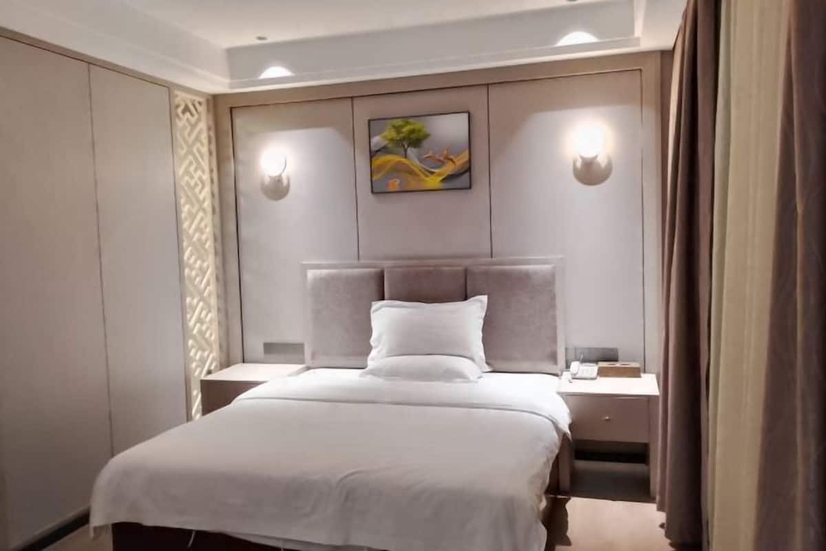 A hotel room with a bed, nightstands, a painting, and wall sconces.